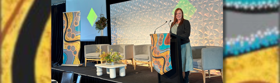 Woman speaking at decorated conference stage with chairs