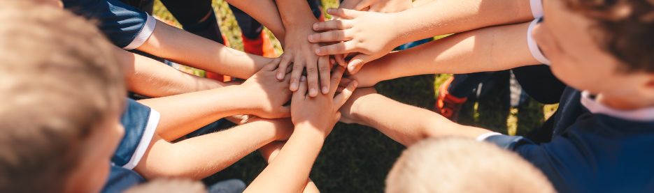 Children stacking hands in team huddle outdoors