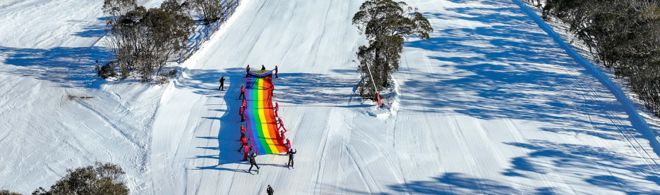 Skiers carrying a rainbow flag on snowy slope